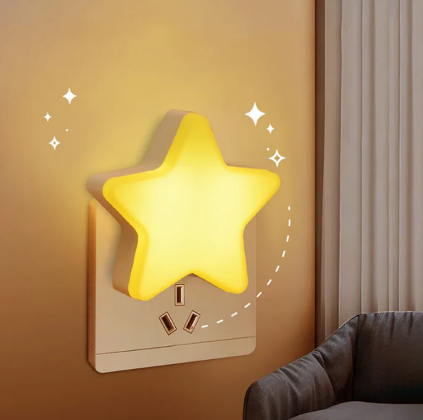 Cute star shaped LED plug-in night light glowing warm white on a bedroom wall